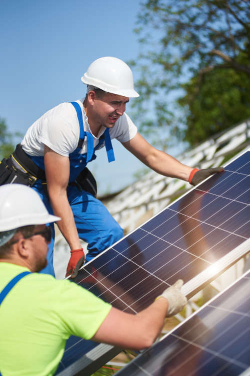 Image of two professional technicians adjusting heavy solar photo voltaic panel to metal platform on blue sky background. Stand-alone solar panel system installation, efficiency and professionalism concept.