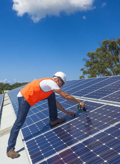 Image of a solar technician installing solar panels on factory roof