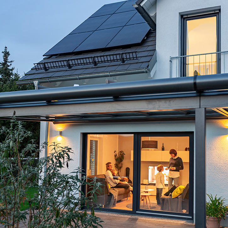 Image showing a view into house through french doors showing a cosy setting. On the roof you can see three rows of REC Solar Panels.
